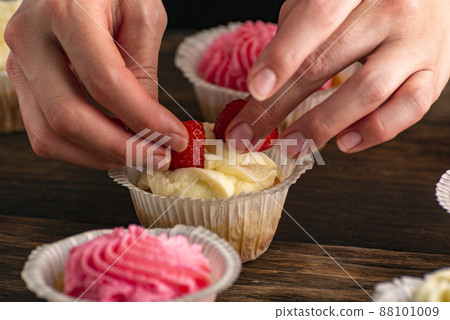 Pastry chef decorates the muffins with fresh strawberries . Cupcakes with berries. Close up. 88101009