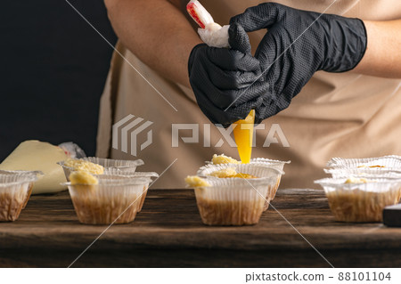 Pastry chef fills muffins with yellow jam. Process of making cupcake by hand. Pastry chef fills muffins with yellow jam. Process of making cupcake by hand. 88101104