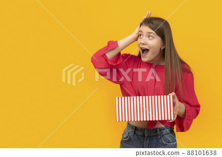 Surprised and overwhelmed girl with gift box in her hands on yellow background. Unexpected gift. 88101638