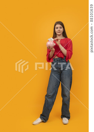 Full-length portrait of young woman with piggy bank and money on yellow background. Financial planning, savings. Full-length portrait of young woman with piggy bank and money on yellow background. Financial planning, savings. 88101639