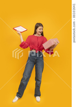 Full-length portrait of brunette girl with gift box on bright deep yellow background. Concept of gifts and surprises. 88101641