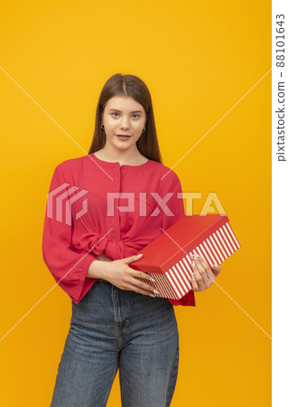 Portrait of teenage girl in red blouse with gift box in her hands on bright yellow background. Vertical frame. Portrait of teenage girl in red blouse with gift box in her hands on bright yellow background. Vertical frame. 88101643