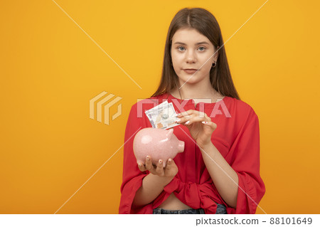 Young woman putting dollar bill in piggy bank on yellow background. Financial planning, savings. 88101649