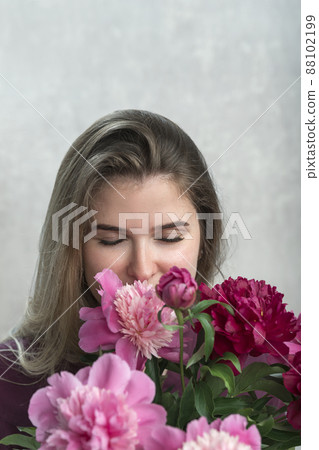 Attractive young woman with brown hair enjoys smell of peonies. Girl with natural beauty with bouquet of peonies. Vertical frame. Attractive young woman with brown hair enjoys smell of peonies. Girl with natural beauty with bouquet of peonies. Vertical frame. 88102199