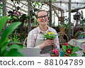 Young woman sells flowers and seedlings via video link on laptop via the Internet. Gardening, sales 88104789