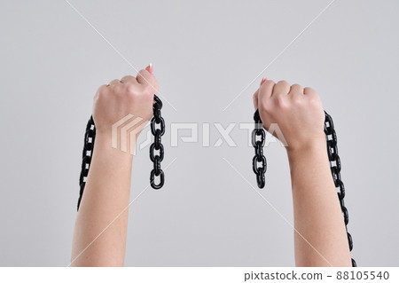 Female hands holding a broken metal chain over grey background with copy space 88105540