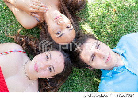 Group of happy teenagers friends relaxing on green grass in meadow and showing peace sign Group of happy teenagers friends relaxing on green grass in meadow and showing peace sign 88107024