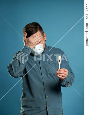 Young man in casual cloth wearing medical protective mask excited, stressed and frightened after read very high temperature result from digital thermometer, illness concept 88107367