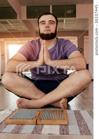 Man exercising yoga meditating sitting hands joined on the floor near sadhu board Man exercising yoga meditating sitting hands joined on the floor near sadhu board 88107445