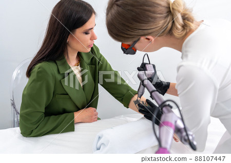 Cosmetologist using laser device to remove an unwanted tattoo from female arm. Concept of erasing tattoos as an expensive procedure in a cosmetology clinic Cosmetologist using laser device to remove an unwanted tattoo from female arm. Concept of erasing tattoos as an expensive procedure in a cosmetology clinic 88107447