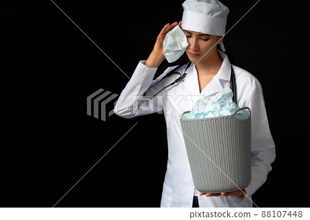 Doctor holding bucket full of used facial masks, throwing them away as symbol of epidemic ending 88107448