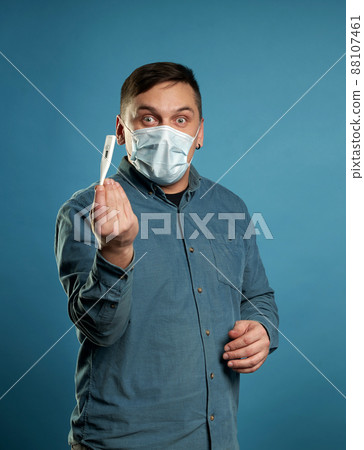 Young man in casual cloth wearing medical protective mask excited, stressed and frightened after read very high temperature result from digital thermometer, illness concept Young man in casual cloth wearing medical protective mask excited, stressed and frightened after read very high temperature result from digital thermometer, illness concept 88107461