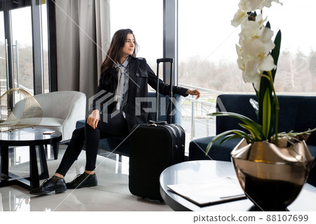 Woman sitting with suitcase in hotel lobby or in an airport lounge 88107699