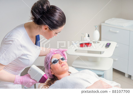 Young woman receiving laser treatment in cosmetology clinic. Eyes covered with protection glasses Young woman receiving laser treatment in cosmetology clinic. Eyes covered with protection glasses 88107700
