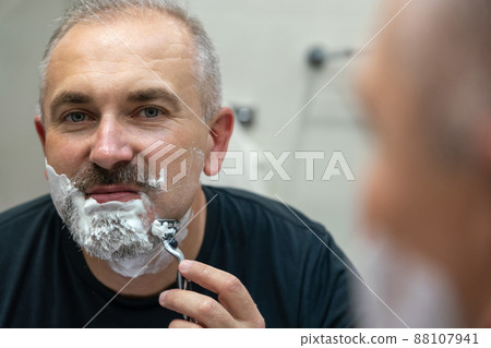Middle aged handsome man shaving his beard in bathroom Middle aged handsome man shaving his beard in bathroom 88107941