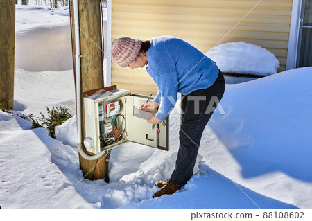 An outdoor switchboard with an electric meter, woman taking readings. 88108602