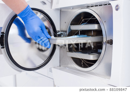Assistant's hand in gloves insert packaged dental instrument to the autoclave to sterilise. 88109847