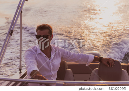 A determined senior businessman in casual clothes and sunglasses enjoys his vacation driving a luxury boat at sunset. Selective focus  88109995