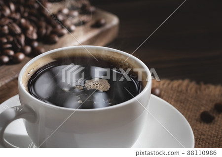 White cup of fresh hot coffee and coffee beans on wooden board on table, close up 88110986