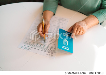 50 60s Caucasian woman hand write with a pen in PESEL document on white table at state service department 50 60s Caucasian woman hand write with a pen in PESEL document on white table at state service department 88112040