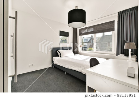 The interior of a bedroom with a bed, a workplace and a small TV near a large window in a modern apartment 88115951