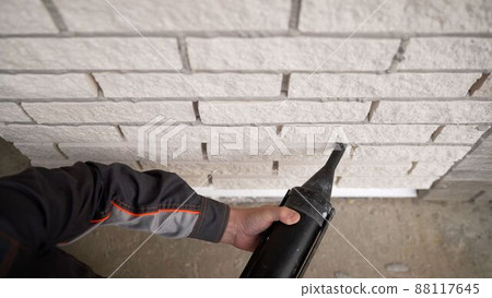 Filling the joints between bricks on the facade of the house. Poor quality brickwork. Cement joints between masonry elements. A worker rubs seams on the facade of a building. Seam filling. 88117645