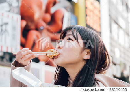 A woman eating takoyaki in Minami, Osaka - Stock Photo [88119433