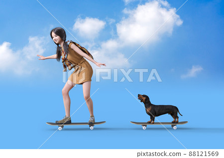 一個女孩和一個黑棕褐色臘腸男孩在陽光明媚的藍天下玩滑板 一個女孩和一個黑棕褐色臘腸男孩在陽光明媚的藍天下玩滑板 88121569