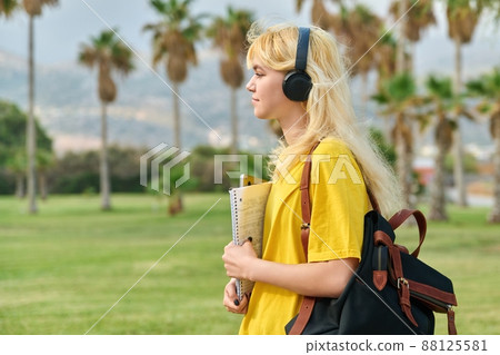 Outdoor portrait of teenage female student in headphones with laptop backpack 88125581