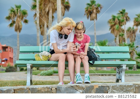 Two girls sisters, teenage and preteen look at a smartphone 88125582