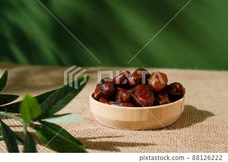 dried dates in a wooden plate on a green background on a sunny day. dried dates in a wooden plate on a green background on a sunny day. 88126222