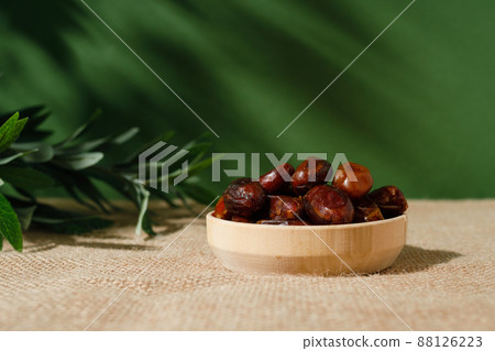 dried dates in a wooden plate on a green background on a sunny day. dried dates in a wooden plate on a green background on a sunny day. 88126223