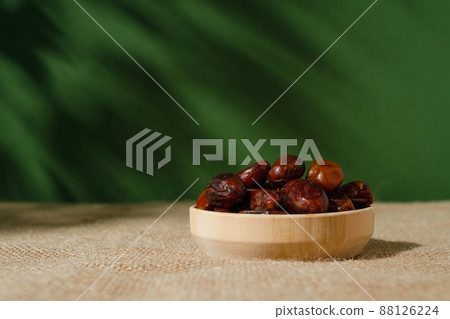 dried dates in a wooden plate on a green background on a sunny day. 88126224