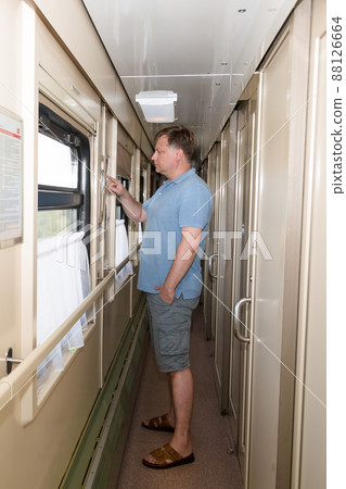 A male train passenger stands in the carriage corridor and reads the route and timetable A male train passenger stands in the carriage corridor and reads the route and timetable 88126664