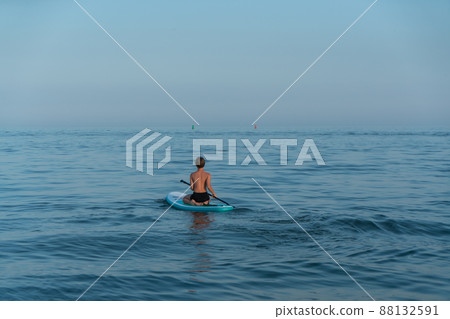 A boy of 11 years old swims on a SUP board in the sea after sunset. 88132591