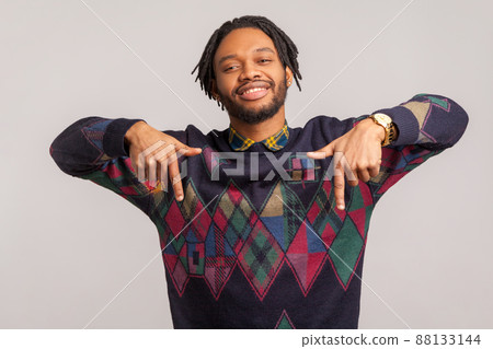 Cheerful satisfied african man with trendy dreadlocks pointing fingers down, paying attention to advertising area, blogger recommending to subscribe. Indoor studio shot isolated on gray background 88133144