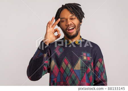 Extremely satisfied bearded african man with dreadlocks showing ok sign with self-confident facial expression, everything is fine, approval. Indoor studio shot isolated on gray background 88133145
