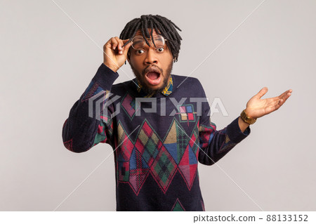 Extremely amazed and shocked african man with beard and dreadlocks looking at camera with widely opened eyes and mouth, surprised and confused with news. Indoor studio shot isolated on gray background 88133152