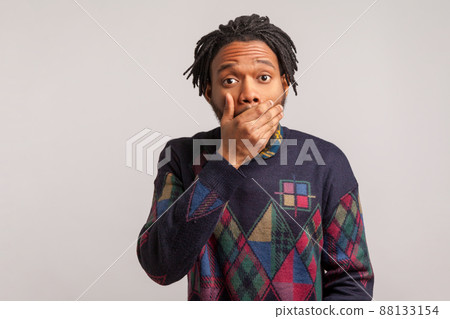 Afraid african man with dreadlock closing mouth with hand looking at camera with big eyes, keeping secret, shocked wondered with news. Indoor studio shot isolated on gray background 88133154