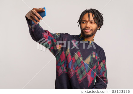 Funny african man with dreadlocks and beard holding smartphone in hand and posing at camera making selfie, camera application. Indoor studio shot isolated on gray background Funny african man with dreadlocks and beard holding smartphone in hand and posing at camera making selfie, camera application. Indoor studio shot isolated on gray background 88133156