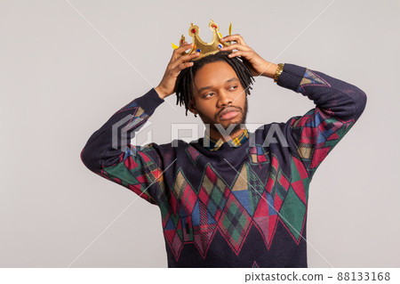 Egocentric self confident african man with dreadlocks trying on crown on his head, imagining himself king, leadership. Indoor studio shot isolated on gray background Egocentric self confident african man with dreadlocks trying on crown on his head, imagining himself king, leadership. Indoor studio shot isolated on gray background 88133168