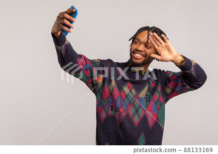 Happy cheerful african man in stylish sweatshirt with dreadlocks posing at camera with toothy smile, blogger saying hi to subscribers, live broadcast. Indoor studio shot isolated on gray background Happy cheerful african man in stylish sweatshirt with dreadlocks posing at camera with toothy smile, blogger saying hi to subscribers, live broadcast. Indoor studio shot isolated on gray background 88133169