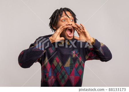 Scared concerned african man with dreadlocks loudly screaming holding hands near widely opened mouth, fear, protest. Indoor studio shot isolated on gray background 88133173