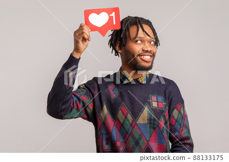 Satisfied wondered african guy looking at like counter button, smiling with pleasure, rejoicing and amusing with popularity on internet, social network. Indoor studio shot isolated on gray background 88133175