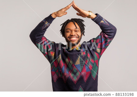 Extremely satisfied african man with dreadlocks showing house gesture holding hands above head with toothy smile on face, real estate agency. Indoor studio shot isolated on gray background 88133198