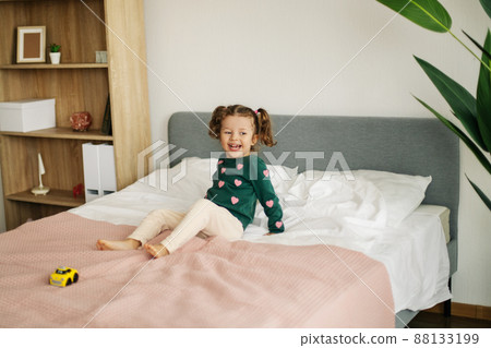 A charming little girl is playing with a car on the bed and fooling around 88133199