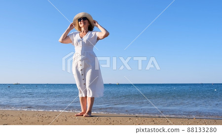 woman in a straw hat and white dress walks along the seashore and admires the blue sea on a sunny woman in a straw hat and white dress walks along the seashore and admires the blue sea on a sunny 88133280