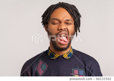 Closeup face of bearded african man with dreadlocks fooling face and grimacing feeling unpleasant taste or smell, disgust. Indoor studio shot isolated on gray background Closeup face of bearded african man with dreadlocks fooling face and grimacing feeling unpleasant taste or smell, disgust. Indoor studio shot isolated on gray background 88133302