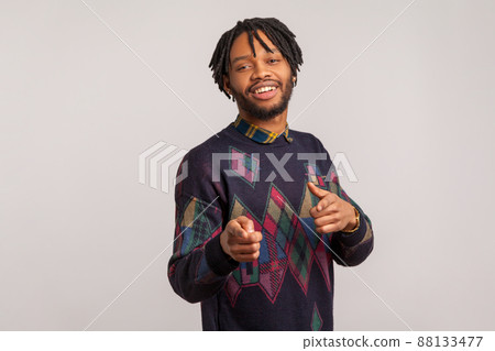 Hey you. Satisfied handsome guy with dreadlocks pointing fingers at camera and looking with toothy smile, flirting, admiring. Indoor studio shot isolated on gray background 88133477