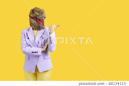 Funny woman wearing rubber mask of dinosaur or reptile shows copy space on yellow background. 88134115